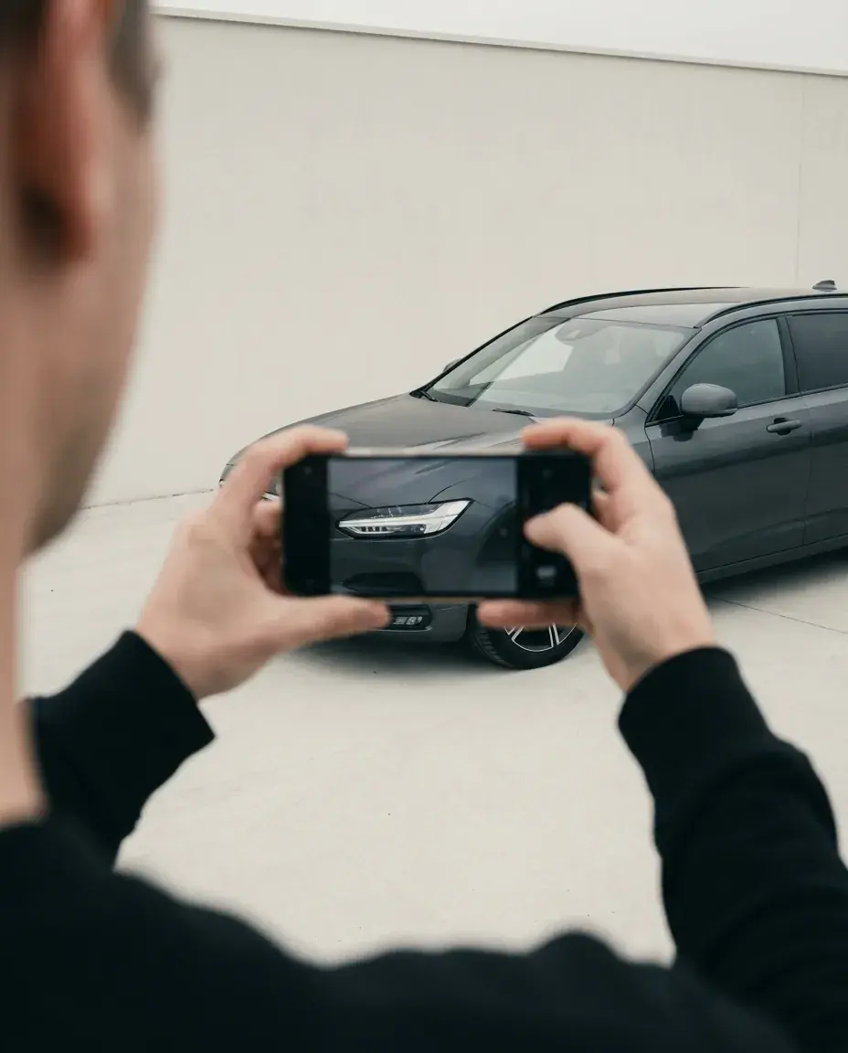 Person fotograferer forhjørnet af en bil med sin telefon.